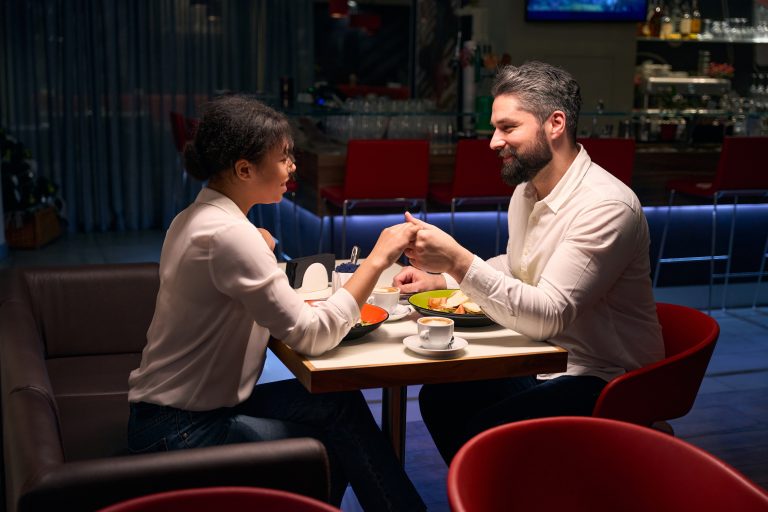 Smiling happy man and his female companion holding hands and looking at each other at restaurant table