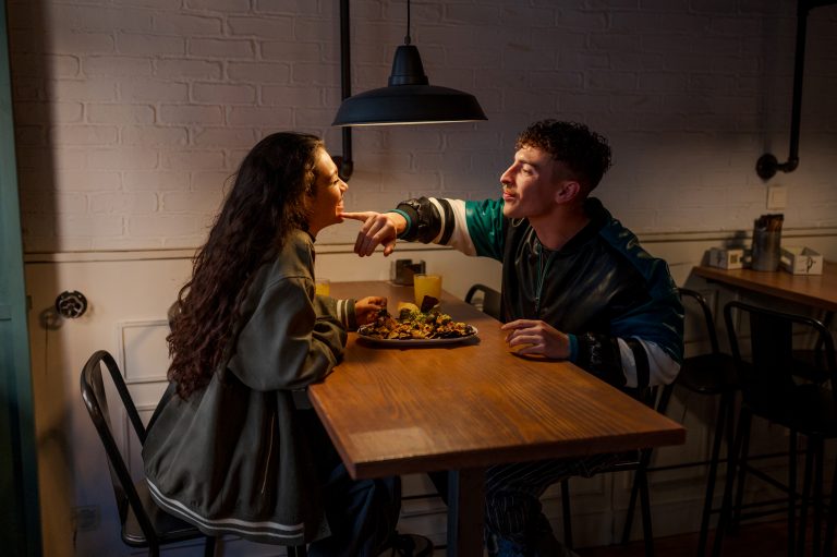 Young man removes leftover food from his girlfriend's mouth while eating together during a romantic date at a restaurant